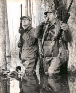 Two men in waders standing next to a tree.