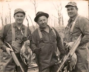 Three men holding guns and a bird in their hands.