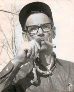 A man with glasses and a hat smoking.
